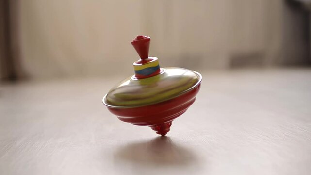 Colorful metal spinning top balancing in motion on a wooden floor with soft light

