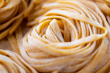 Close-up of raw fettuccine pasta nests, with intricate folds and a dusting of flour. The image...