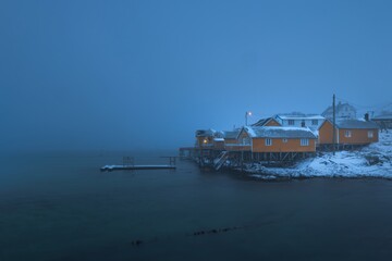 Sakrisøy auf den Lofoten in Norwegen zur blauen Stunde unter dichter Nebeldecke, der Fjord liegt...