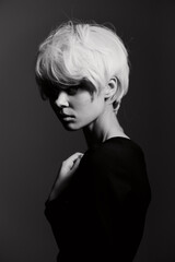 Stylish young woman with short platinum hair, looking thoughtfully into the distance against a dark monochrome background. Fashion and beauty concept.