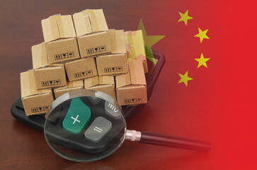 Check import tariffs of China. Many carton boxes on calculator under magnifying glass and Chinese...