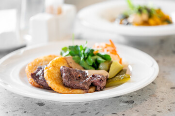 A plate features juicy slices of steak paired with crispy potato patties and fresh vegetables. The elegant presentation highlights the delicious combination of flavors in a gourmet meal.