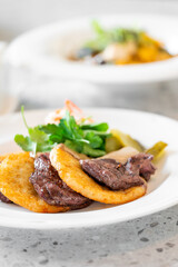 A close-up of a plate showcases tender steak slices accompanied by crispy potato patties and fresh greens. The presentation emphasizes a delicious blend of flavors in a gourmet meal setting.