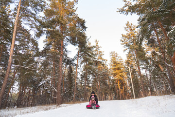 Father and daughter having fun with snow tube in the forest