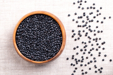 Beluga lentils in a wooden bowl on linen. Dried variety of a small, black lentil, Lens esculenta, also known as caviar lentils. They are high on fiber and protein, of nutty aroma and earthy flavor.
