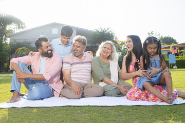 Multi Generation-Happy Indian family sitting together outside their house. Parents grandparents and...