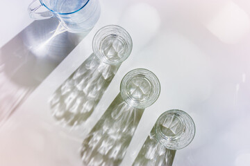 Water Glass with shadows at sunlight on white, delicate violet blue color, minimal aesthetic top view shiny glasses at natural light, summer drink concept, pastel gradient interplay light and shadow