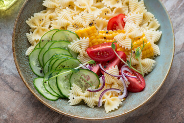 Rustic plate with farfalle, cucumber, tomatoes and sweet corn pasta salad, horizontal shot, middle...