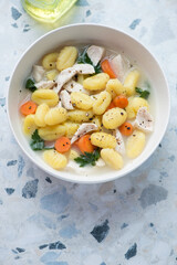 Bowl of chicken soup with potato gnocchi on a white and blue granite background, vertical shot, high angle view