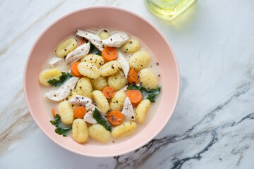 Roseate bowl with creamy chicken gnocchi soup, horizontal shot on a white stone background, top view