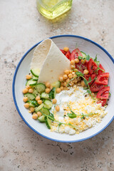 Plate with yogurt, cucumber, tomatoes, chickpeas and grated egg, vertical shot on a beige granite background, high angle view