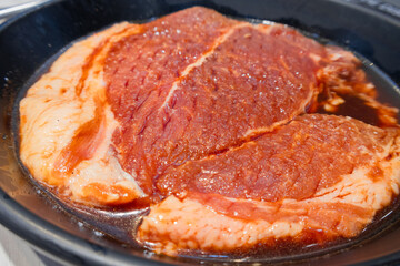 A raw pork chop drenched in sauce on a black flat skillet. ready to cook restaurant concept