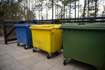 Three colored garbage bins for waste separation placed on outdoor pavement