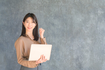 ノートパソコンを持ってガッツポーズをする日本人女性