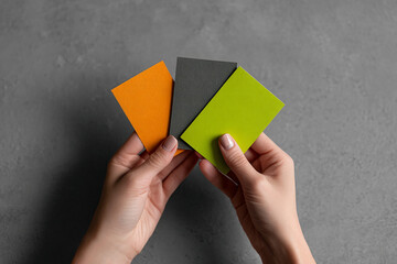 Hands holding three textured cards: orange, gray, and lime green.  Showcase of color palettes, ideal for branding or design inspiration