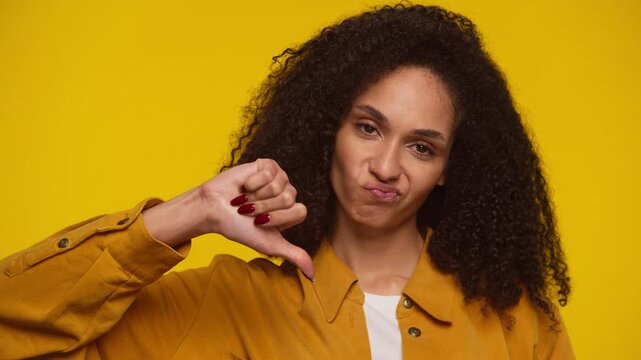 Woman Giving Thumbs Down Disapproval Gesture on Yellow Background