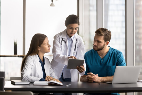 Mentorship in healthcare. Smiling young woman doctor mentor supervisor teach diverse couple interns explain mentees diagnosis using patient health data electronic xray image on digital tablet screen