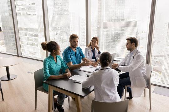 Professional seminar. Confident young man surgeon diverse medical team leader speak to doctors group on briefing workshop round table meeting instruct colleagues consult on surgery details. Copy space