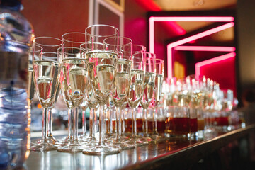 A beautiful row of elegant champagne glasses has been meticulously lined up on a stylish bar, ready...