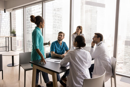 Teamwork for patient health. Diverse medical team multiethnic doctors of different specialities gather at table for discussion listen to young female colleague nurse surgeon giving professional advice