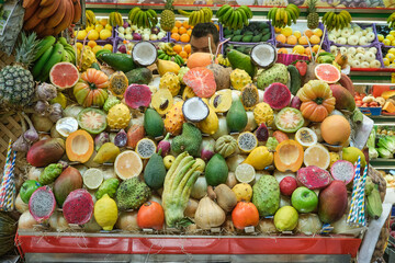 Vibrant and colorful arrangement of exotic tropical fruits displayed at a local market stall. The variety includes dragon fruit, papaya, coconut, avocado, cherimoya, passion fruit, citrus, and more, s