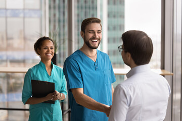 Business and medicine collaboration. Happy young male doctor shake hand of businessman at clinic...