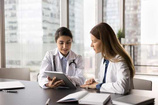 Interactive learning in medicine. Skilled millennial female doctor therapist physician mentoring teaching young girl student intern at clinic workplace explain medical problem on digital tablet screen