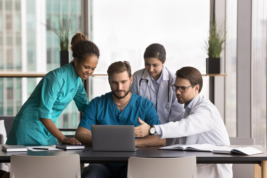 Technology in medicine. Diverse doctors group stand around lead physician surgeon using notebook look on screen review electronic xray mri ct scan make collaborative decision about patient diagnosis