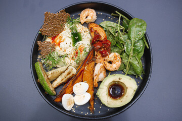 A beautifully arranged black plate filled with an enticing variety of food including succulent shrimp, fluffy eggs, creamy avocado, and fresh spinach leaves