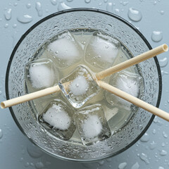 Refreshing drink with ice cubes and two straws on a gray surface  