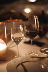 Two elegant wine glasses are beautifully resting on a table, positioned gracefully beside a flickering candle that enhances the ambiance