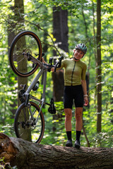 Fototapeta premium Female cyclist, dressed in cycling outfit and helmet, stands with her gravel bike on fallen log in forest. This scene represents adventure, outdoor activity, and healthy lifestyle.