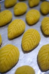 Close-up of traditional Middle Eastern or Mediterranean cookies with intricate leaf-like patterns, arranged on a metal baking tray. The golden dough appears fresh and unbaked.