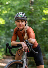 Blonde-haired young cyclist smiles as she stands with gravel bike park. Concept healthy lifestyle,...
