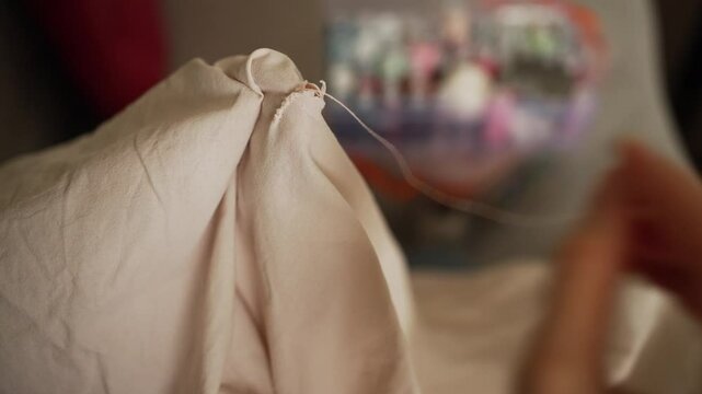 Skilled seamstress hands performing intricate gathering stitch on delicate white fabric, sewing kit softly blurred in background, showcasing precision craft technique