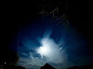 Night sky with bright moon and dramatic clouds illuminated in silhouette