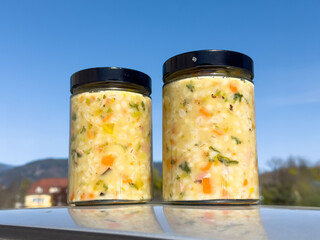 Jars of homemade vegetable ritschert suppe set against a clear blue sky