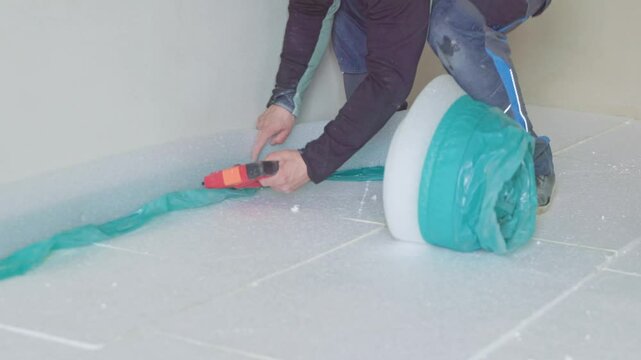 Construction worker installing vapor barrier film on insulated floor