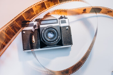 Vintage film camera lying on a white background with a curled strip of film reel wrapped around, evoking memories of classic photography and traditional darkroom techniques