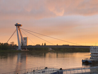 Fototapeta premium Modern cable-stayed bridge with UFO-style tower over calm river at sunset in Bratislava, Slovakia.