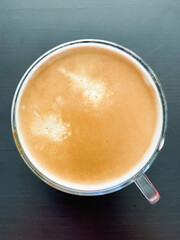 Top view of glass cup with freshly made coffee on dark wooden table.