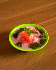 Traditional Indonesian Iced Grass Jelly Dessert with Coconut Milk and Palm Sugar Syrup Served in a Bowl for a Refreshing Sweet Treat.