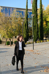 Executive woman walking with briefcase and smartphone in front of office building