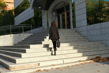 Executive woman from behind climbing stairs to enter modern office building
