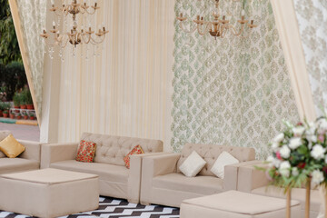 Elegant event space with neutral seating, patterned backdrop, and crystal chandeliers for a...