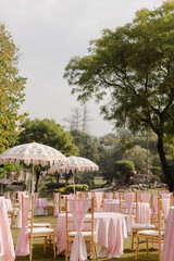 Outdoor event with pink decor, round tables, and parasols. Lush green background for an elegant and festive occasion.