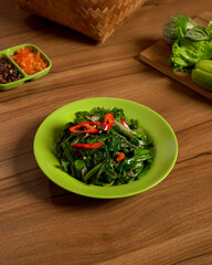 Stir-Fried Genjer Greens Served with Fresh Raw Vegetables and Spicy Sambal on the Side, A Traditional Indonesian Vegetable Delicacy.
