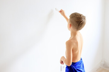 A young boy renovating a room, sanding the walls with sandpaper and painting them white with a...