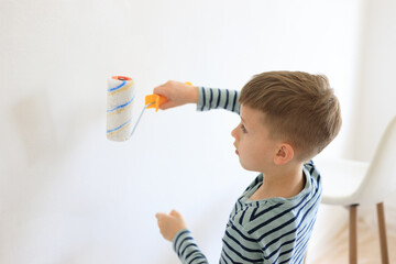 A young boy renovating a room, sanding the walls with sandpaper and painting them white with a...