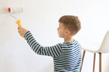 A young boy renovating a room, sanding the walls with sandpaper and painting them white with a roller. Home improvement and DIY repair concept